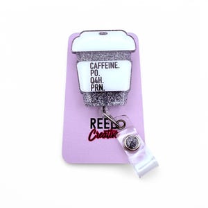 May include: Silver glitter coffee cup badge reel with a white background and the text "CAFFEINE. PO. Q4H. PRN."  The badge reel is attached to a clear plastic strap with a silver glitter button.