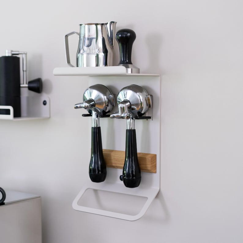 May include: White metal wall mounted coffee station with two chrome portafilters, a wooden shelf, and a silver pitcher.
