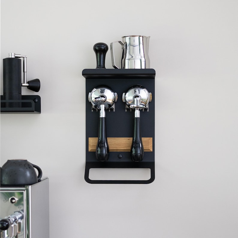 May include: Black metal wall-mounted coffee accessory holder with two chrome portafilters, a wooden shelf, and a handle.