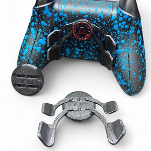 Könnte beinhalten: Ein schwarzer und blauer Videospiel-Controller mit einem blauen Spritzmuster. Der Controller hat einen schwarzen und grauen Aufsatz auf der Rückseite und einen schwarzen und grauen Aufsatz auf der Vorderseite. Der Aufsatz auf der Vorderseite hat den Text "V3D1" aufgedruckt.