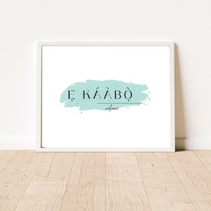 May include: A white framed print with a light blue watercolor-style background and the text "E KÄÄBÖ welcome" in black.