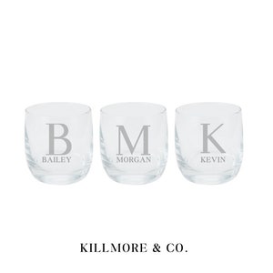 May include: Three clear, stemless glasses, each engraved with a letter and name: "B" for Bailey, "M" for Morgan, and "K" for Kevin. The glasses are displayed on a white backdrop. The text "KILLMORE & CO." is at the bottom.