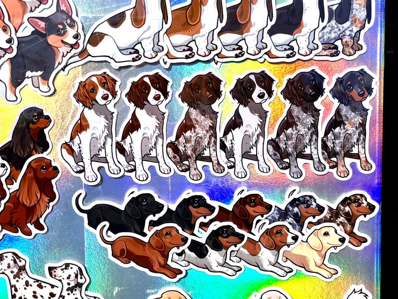 May include: A collection of colorful dog breed stickers featuring various breeds, including a corgi, dachshund, Brittany spaniel, and a few others. The stickers are on a holographic background.