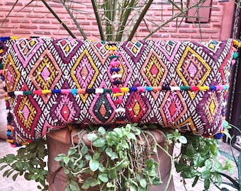 May include: A rectangular throw cushion featuring a vibrant, multi-coloured diamond pattern in shades of pink, yellow, green, and purple. The fabric is heavily textured with intricate embroidery and small colourful pom-poms along the edges.