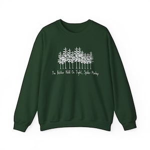 May include: A dark green sweatshirt with a white graphic of a forest of trees. The text "You Better Hold On Tight, Spider Monkey" is printed below the trees in a handwritten style font.