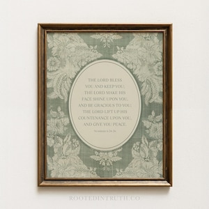 May include: A framed print with a vintage design. The artwork displays an oval central panel with text from Numbers 6:24-26, set against a backdrop of a floral pattern in green and white. The frame is a warm brown colour.