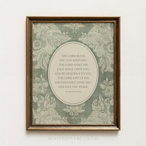 May include: A framed wall art print featuring a sage green background with a white floral lace pattern. In the centre, an oval contains the text: THE LORD BLESS YOU AND KEEP YOU; THE LORD MAKE HIS FACE SHINE UPON YOU, AND BE GRACIOUS TO YOU; THE LORD LIFT UP HIS COUNTENANCE UPON YOU, AND GIVE YOU PEACE. NUMBERS 6:24-26.