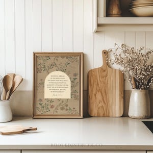 a framed print with a floral design, a wooden cutting board, a vase with flowers, and a shelf with various kitchen items.