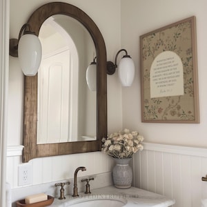 a bathroom with a white sink, a wooden-framed mirror, and a framed Bible verse on the wall.