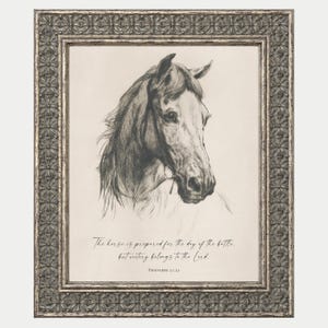 May include: A framed wall art piece featuring a charcoal-style sketch of a horse head. Below the horse, the text reads: The horse is prepared for the day of the battle, but victory belongs to the Lord. Proverbs 21:31. The frame has a metallic finish.