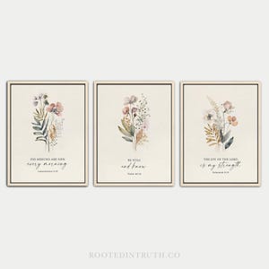 May include: A set of three rectangular wall art prints on a cream background, each featuring a watercolour floral bouquet and black text. The prints display the phrases: His mercies are new every morning, Be still and know, and The joy of the Lord is my strength.