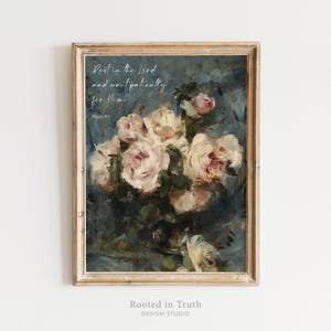 May include: A framed wall art print featuring an oil painting of pale pink and white roses in a dark blue and grey setting. The text reads: Rest in the Lord and wait patiently for Him. Psalm 37:7. The frame is a light wood with a textured finish.