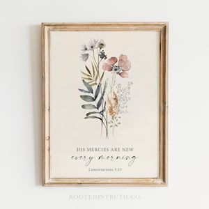 May include: Framed floral art print featuring watercolor flowers in shades of pink, purple, and green. The print includes the text "HIS MERCIES ARE NEW every morning" and "Lamentations 3:23". The frame is a light brown color.