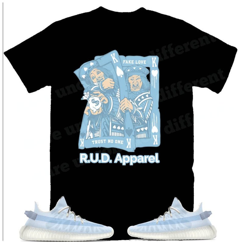 May include: A black t-shirt with a blue graphic of two kings playing cards. The graphic includes the text "Fake Love" and "Trust No One". The t-shirt also has the text "R.U.D. Apparel" printed on it. Two light blue sneakers are also pictured.