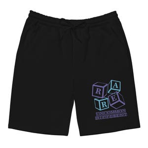 Könnte beinhalten: Schwarze Shorts mit Kordelzug und Taschen. Die Shorts zeigen eine Grafik von gestapelten Würfeln mit den Buchstaben "R", "A" und "E" in einem Farbverlauf aus Blau und Lila. Der Text "UNCOMMON DIFFERENT" befindet sich darunter.