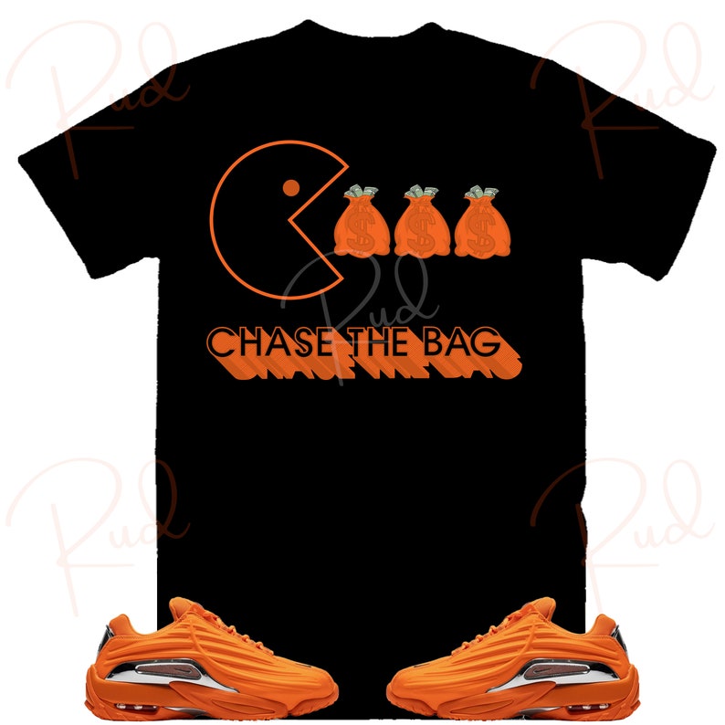 Pode incluir: Camiseta preta com um gr&aacute;fico laranja de Pac-Man comendo tr&ecirc;s sacos de dinheiro laranja com sinais de d&oacute;lar. O texto "CHASE THE BAG" est&aacute; escrito em laranja abaixo do gr&aacute;fico. Tamb&eacute;m &eacute; mostrado um par de t&ecirc;nis laranja com detalhes brancos.