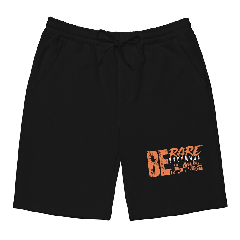 Puede incluir: Pantalones de ch&aacute;ndal negros con cintura el&aacute;stica y un estampado gr&aacute;fico que dice "BE RARE UNCOMMON" en naranja.