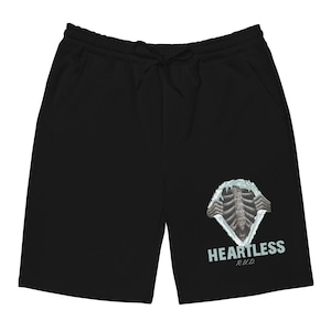 Puede incluir: Pantalones cortos negros con cintura con cordón y bolsillos. Los pantalones cortos presentan un gráfico de una caja torácica rasgando la tela, con la palabra "HEARTLESS" y "R.U.D." impresas debajo.