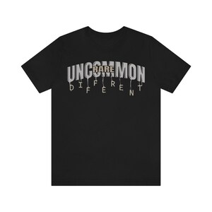 May include: Black t-shirt with the text "UNCOMMON" in white letters with a dripping effect. The word "RARE" is in brown letters and is part of the word "UNCOMMON". The text "DIFFERENT" is below the word "UNCOMMON" in white letters with a dripping effect.