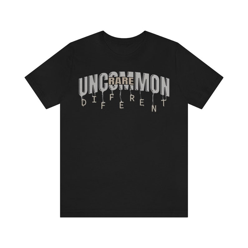 May include: Black t-shirt with the text "UNCOMMON" in white letters with a dripping effect. The word "RARE" is in brown letters and is part of the word "UNCOMMON". The text "DIFFERENT" is below the word "UNCOMMON" in white letters with a dripping effect.