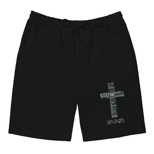 Puede incluir: Pantalones cortos negros con cintura con cordón y bolsillos. Un gráfico de cruz hecho con la palabra "Blessed" está en la pierna derecha. Las iniciales "R.U.D." están debajo.