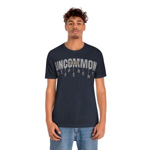 May include: A navy blue t-shirt with the text "UNCOMMON" in white with the word "RARE" highlighted in brown. The text is dripping down the shirt.
