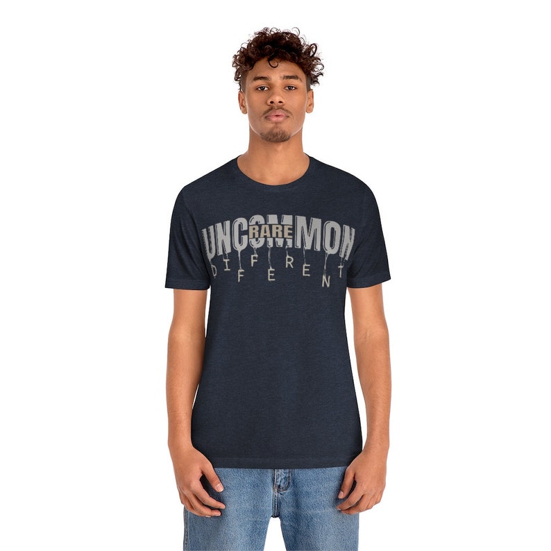 May include: A navy blue t-shirt with the text "UNCOMMON" in white with the word "RARE" highlighted in brown. The text is dripping down the shirt.