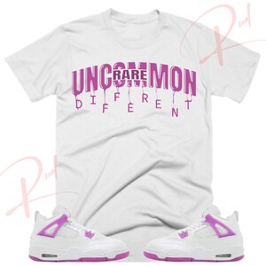 May include: White t-shirt with pink dripping text that reads "Uncommon Rare Different".  White sneakers with pink accents.