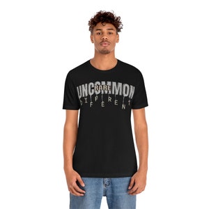 May include: Black t-shirt with a white graphic that says "UNCOMMON RARE DIFFERENT". The word "RARE" is highlighted in brown.