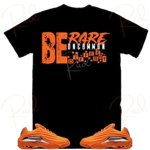 Puede incluir: Una camiseta negra con el texto "BE RARE UNCOMMON" en naranja. El texto est&aacute; en una fuente en negrita y de bloques. La camiseta se combina con un par de zapatillas naranjas con suela blanca.