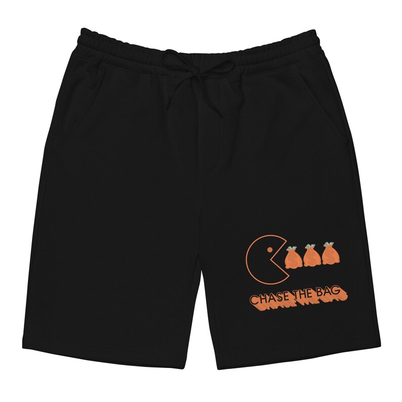 Pode incluir: Cal&ccedil;as de moletom pretas com um gr&aacute;fico de Pac-Man laranja e o texto "CHASE THE BAG" impresso na perna direita.