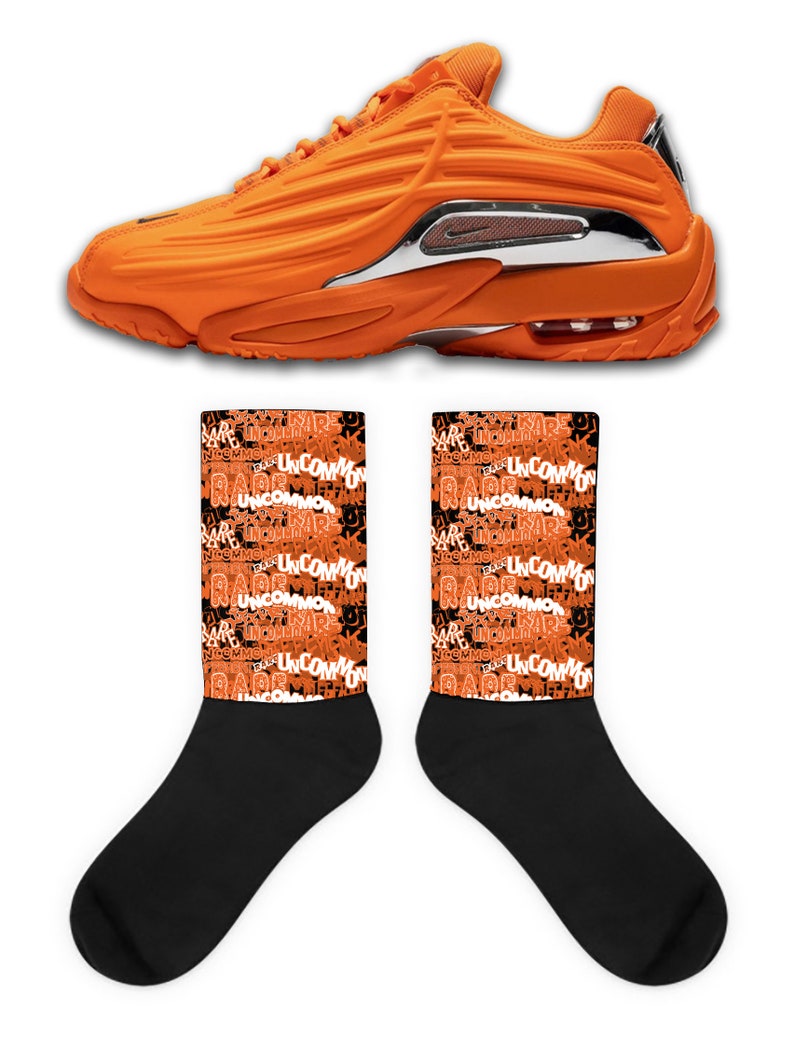 Puede incluir: Un par de zapatillas deportivas naranja y negras con un acento plateado en el tal&oacute;n. Las zapatillas se combinan con calcetines negros que tienen un patr&oacute;n repetido de las palabras "Rare" y "Uncommon" en naranja.
