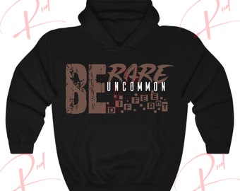 May include: Black hooded sweatshirt with the text "BE RARE UNCOMMON" in brown letters. The text "DIFFERENT" is spelled out in a grid pattern below the main text.