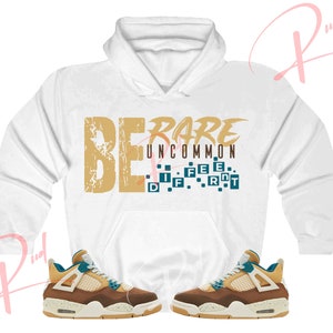 May include: White hoodie with the text "BE RARE UNCOMMON DIFFERENT" in gold and blue. Two brown and blue sneakers with white soles.