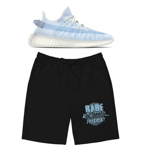 Puede incluir: Un par de pantalones cortos deportivos negros con un estampado gr&aacute;fico azul que dice "RARE UNCOMMON DIFFERENT". Los pantalones cortos se combinan con una zapatilla deportiva azul claro y blanca.