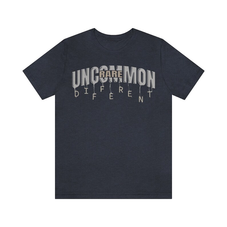 May include: A navy blue t-shirt with the words "Uncommon" and "Rare" printed in white and gray. The word "Rare" is printed in a larger font size and is centered above the word "Uncommon". The word "Different" is printed in smaller letters below the word "Uncommon".