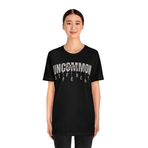 May include: A black t-shirt with a white graphic that reads "Uncommon Rare Different". The graphic is in a dripping font style.