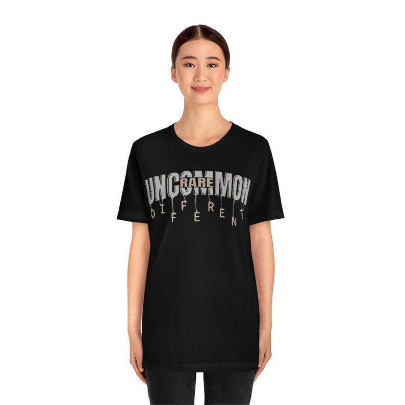 May include: A black t-shirt with a white graphic that reads "Uncommon Rare Different". The graphic is in a dripping font style.