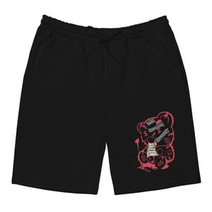 Può includere: Pantaloncini neri con vita con coulisse e tasche. Una grafica rosa di un orsacchiotto che tiene in mano dei soldi è stampata sulla gamba destra. Il testo "RARE UNCOMMON DIFFERENT" è sopra l'orso.