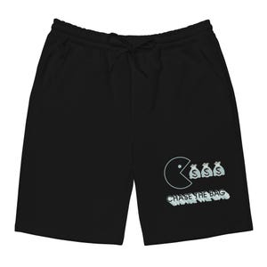 Puede incluir: Pantalones cortos negros con cintura con cordón y bolsillos. Los pantalones cortos presentan un personaje tipo Pac-Man comiendo bolsas de dinero, con el texto "CHASE THE BAG" en una fuente estilizada. El diseño es de color azul claro.