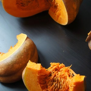 May include: Close-up of a cut orange pumpkin with seeds and flesh visible. The pumpkin is on a dark gray surface.