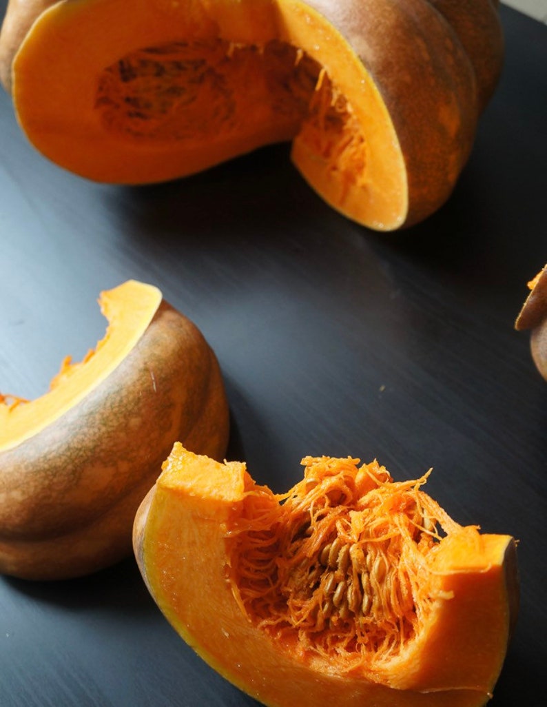 May include: Close-up of a cut orange pumpkin with seeds and flesh visible. The pumpkin is on a dark gray surface.