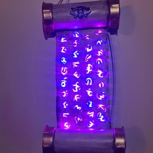 May include: A scroll-shaped wall hanging with glowing purple lights. The scroll has a light grey body with gold-coloured ends. The scroll is covered in symbols and has a blue eye symbol at the top.