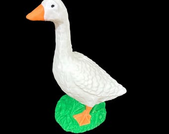 May include: White goose figurine with orange beak and feet, standing on a green base.