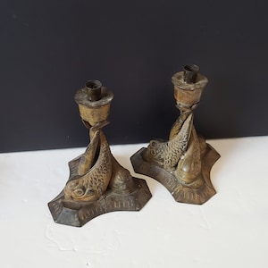 May include: A pair of antique brass candlesticks featuring a fish design. The candlesticks are in good condition and have a pleasing patina.