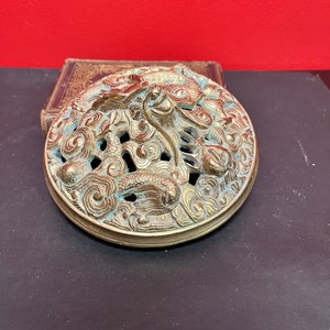 Könnte beinhalten: Ein runder, messingfarbener Räucherofen mit einem komplizierten Design aus einem Drachen und Wolken. Der Räucherofen hat einen erhöhten Rand und eine glatte, polierte Oberfläche.