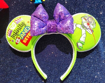 May include: A lime green headband with white trim and two round ears. One ear features Buzz Lightyear, the other reads "To Infinity and Beyond." A sequined purple bow sits atop the headband, and a small alien figure is perched above.