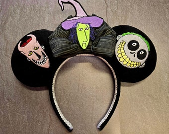 Könnte beinhalten: Schwarzes Mausohren-Stirnband mit gestickten Figuren aus einem Film. Die Ohren zeigen eine Hexe, eine Figur mit Gehirn und einen Totenkopf mit aufgenähtem Lächeln. Das Stirnband ist schwarz mit weißem Besatz.