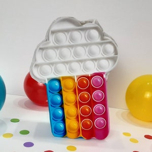 May include: A white cloud-shaped pop-it toy with a rainbow pop-it attached to the bottom. The rainbow pop-it has blue, yellow, orange, and pink sections.