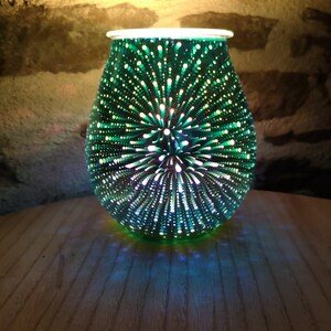 May include: A green glass oil diffuser with a white top and a starburst pattern. The diffuser is lit and casting a blue glow.